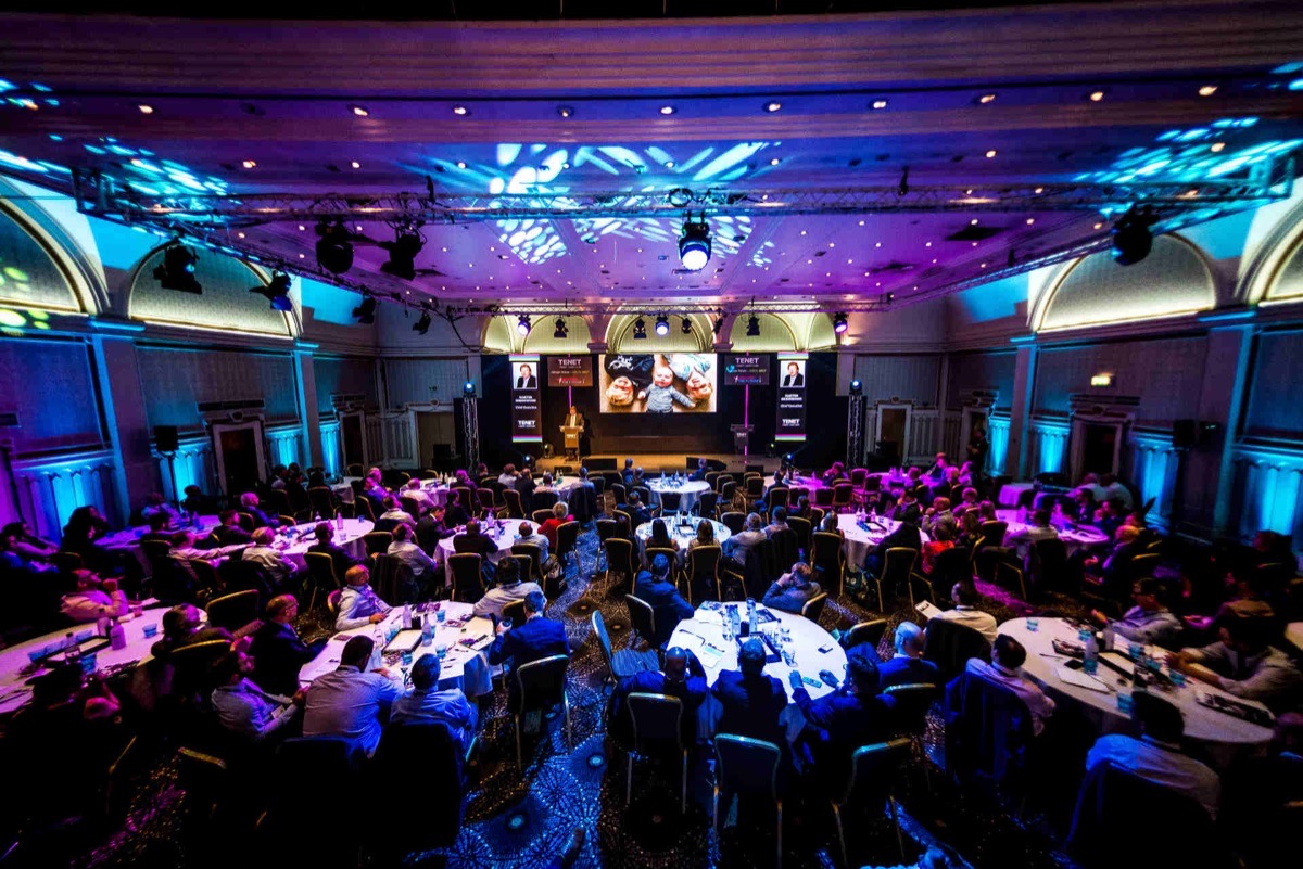 A corporate event in a grand ballroom with stage lighting and seated guests at round tables