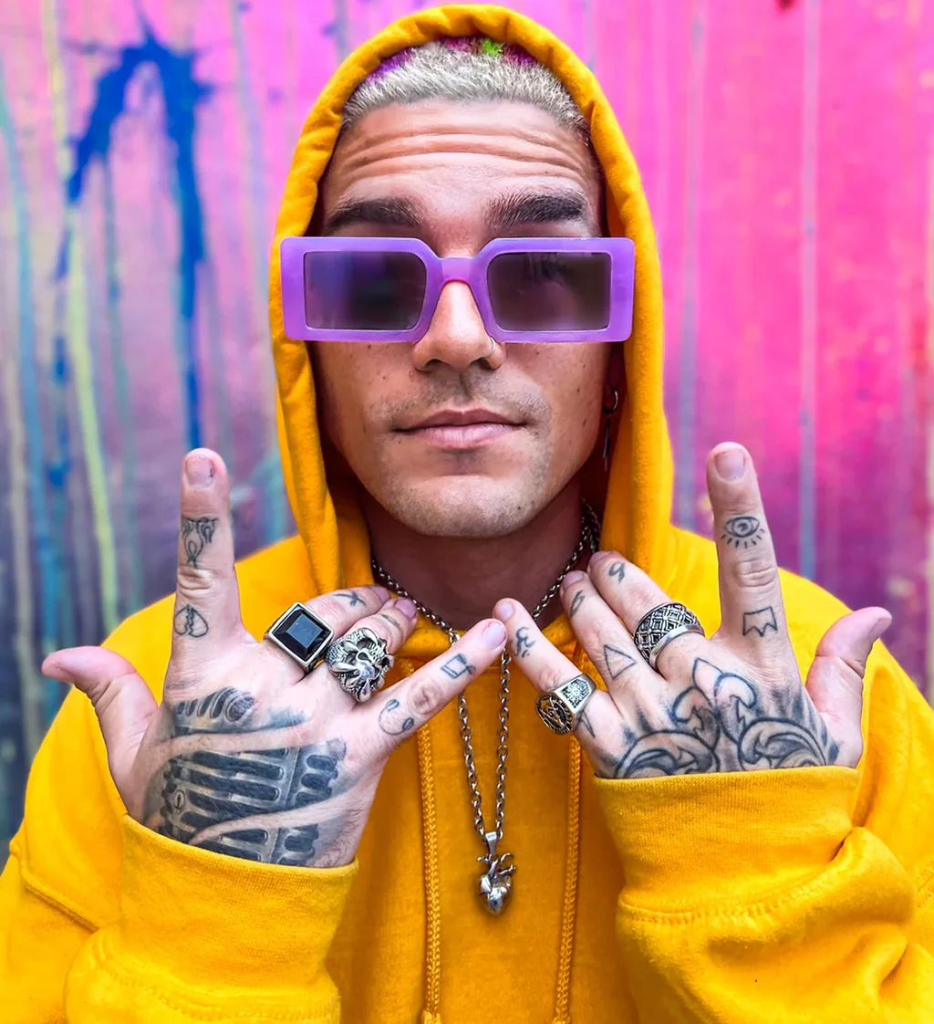 Artist in a yellow hoodie against a vivid painted wall